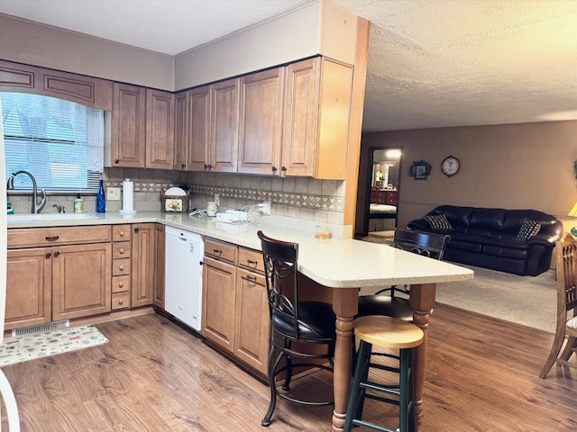 kitchen with a peninsula, light countertops, light wood-style floors, white dishwasher, and a sink