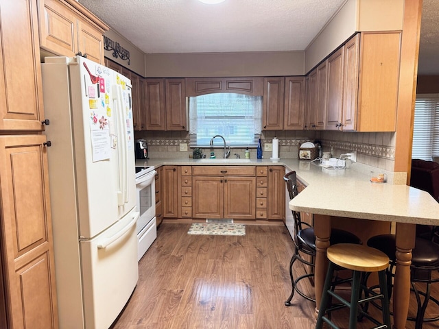 kitchen with a sink, white appliances, a kitchen bar, a peninsula, and light wood finished floors