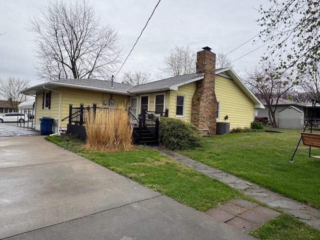 rear view of house with driveway, cooling unit, a chimney, and a lawn