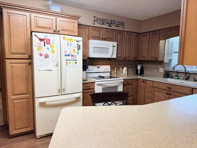 kitchen featuring white appliances, wood finished floors, light countertops, a sink, and backsplash