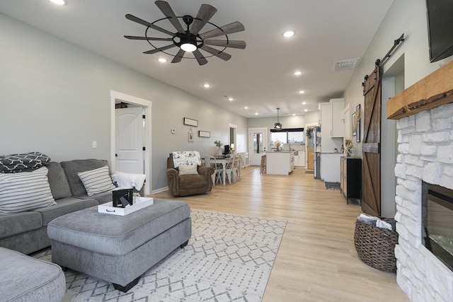 1798 E 328th Rd, Bolivar, MO 65613 - living room featuring ceiling fan, a stone fireplace, recessed lighting, a barn door, and light wood finished floors