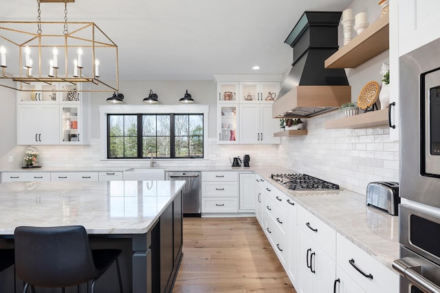 kitchen with open shelves, a sink, appliances with stainless steel finishes, light wood finished floors, and custom range hood