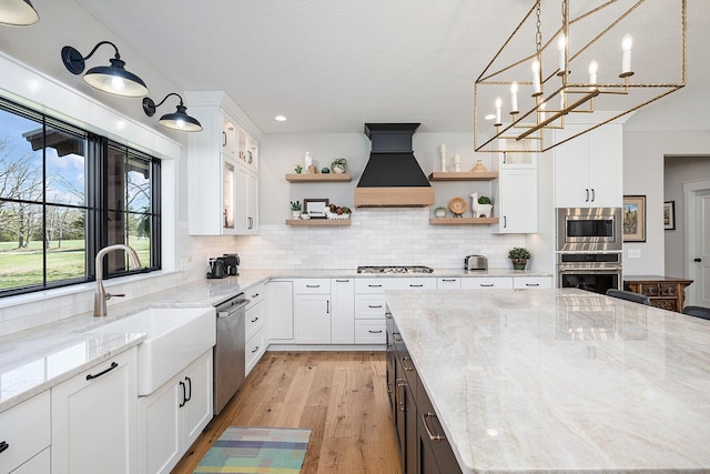 kitchen with premium range hood, open shelves, white cabinets, appliances with stainless steel finishes, and a sink