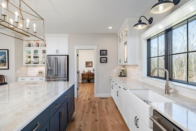 kitchen with light wood-type flooring, white cabinetry, blue cabinets, a sink, and stainless steel appliances