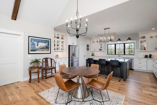 dining room with light wood-style flooring, a chandelier, and lofted ceiling with beams
