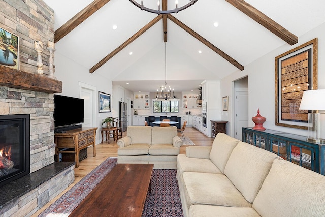 living room featuring beamed ceiling, a stone fireplace, a notable chandelier, and light wood-style floors