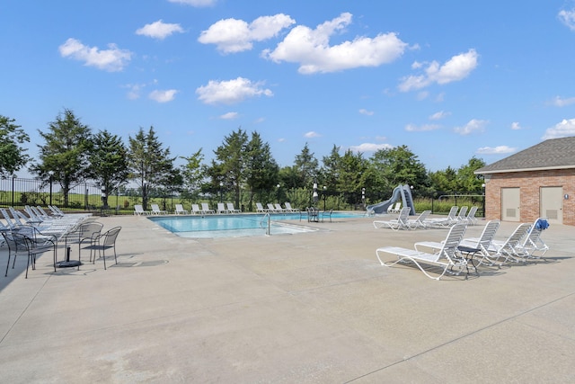 community pool with fence, a water slide, and a patio