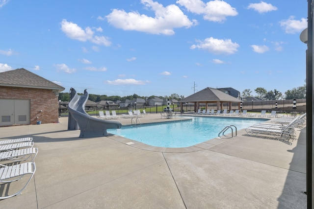pool featuring a water slide, fence, and a patio