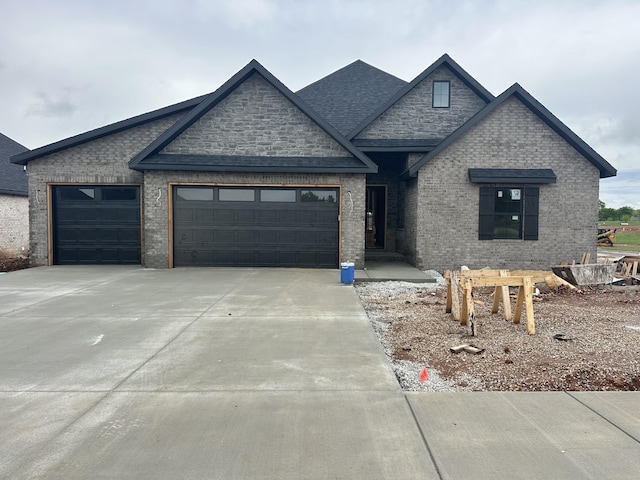 view of front facade featuring a garage, a shingled roof, concrete driveway, and brick siding