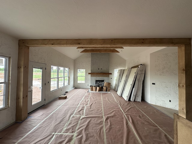 living room featuring vaulted ceiling with beams, a textured wall, and a fireplace