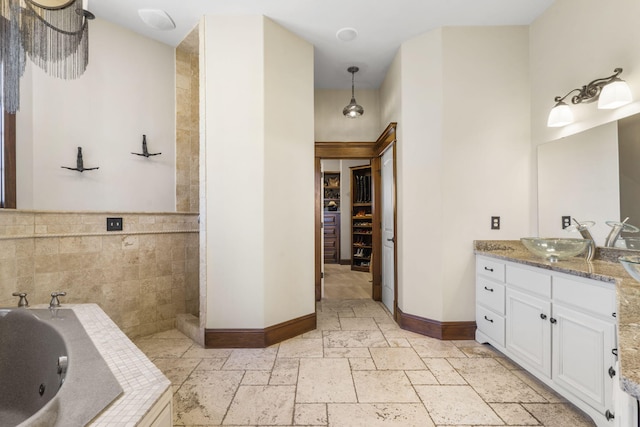 bathroom with a whirlpool tub, vanity, baseboards, a walk in closet, and stone tile floors
