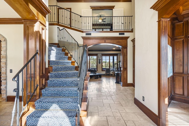 foyer with arched walkways, a towering ceiling, stairs, baseboards, and stone tile flooring
