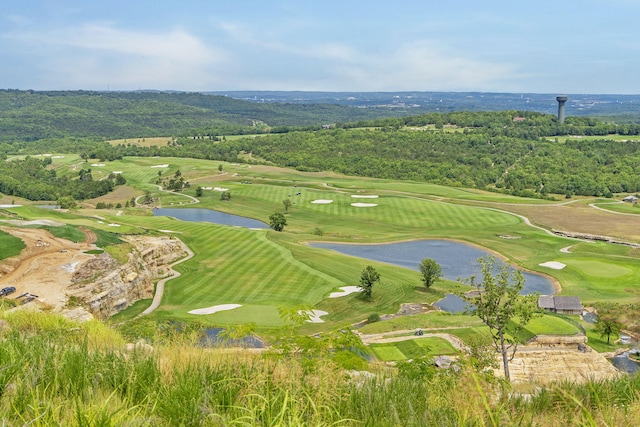 drone / aerial view featuring view of golf course, a view of trees, and a water view