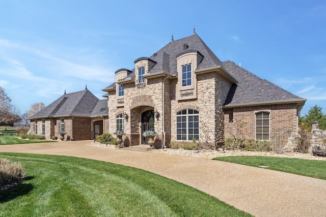 french country inspired facade featuring brick siding, a shingled roof, stone siding, and a front lawn