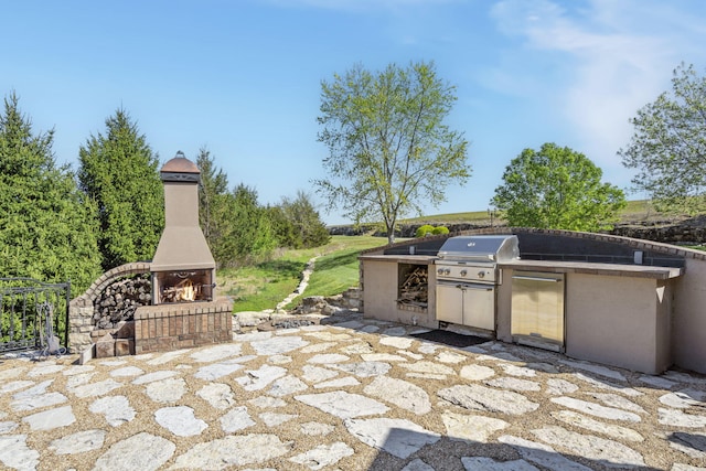 view of patio / terrace featuring a warm lit fireplace, a grill, and exterior kitchen