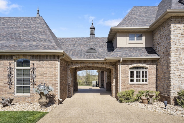 exterior space featuring brick siding and roof with shingles