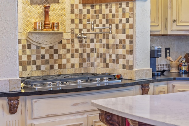kitchen with a textured wall, stainless steel gas stovetop, backsplash, and cream cabinetry