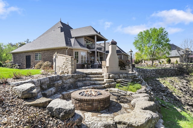 rear view of property featuring a patio area, an outdoor fire pit, a balcony, brick siding, and roof with shingles