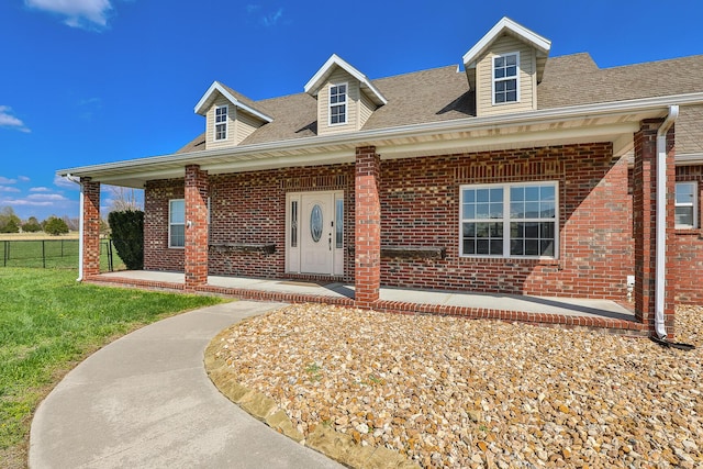 new england style home with roof with shingles, brick siding, fence, and covered porch