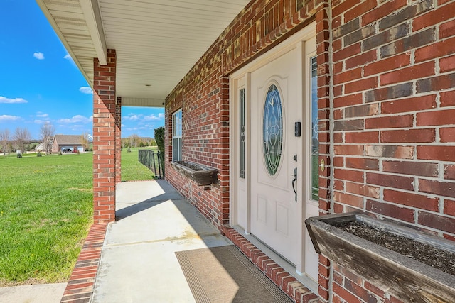 view of exterior entry featuring brick siding, covered porch, and a lawn