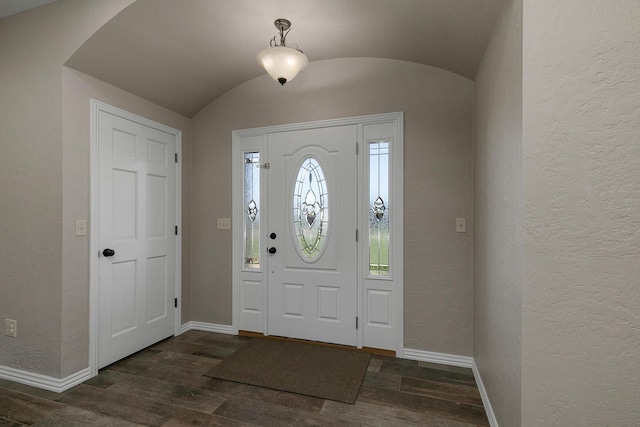 foyer featuring a textured wall, dark wood-type flooring, baseboards, and vaulted ceiling