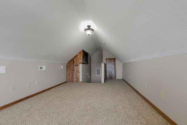 bonus room with a textured ceiling, carpet flooring, lofted ceiling, and visible vents