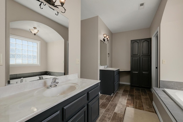 full bath with two vanities, wood finish floors, a bath, visible vents, and a sink