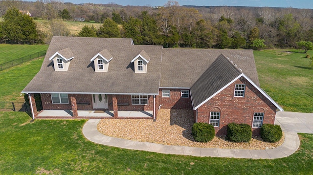 view of front of home with a front yard, brick siding, fence, and a shingled roof