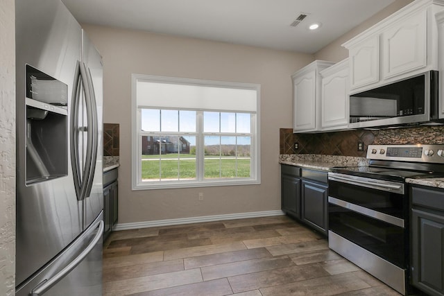 kitchen with tasteful backsplash, white cabinets, visible vents, stainless steel appliances, and dark wood-style floors