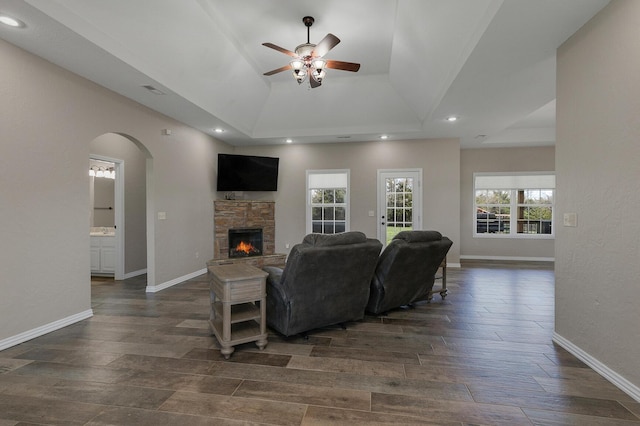 living area with dark wood-style flooring, ceiling fan, baseboards, and a fireplace