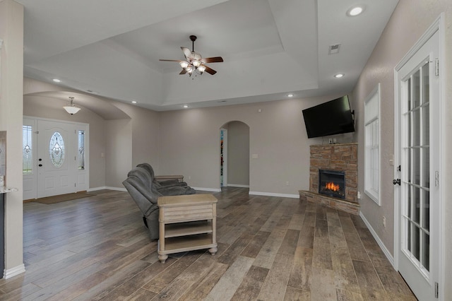 living area featuring ceiling fan, a tray ceiling, arched walkways, wood finished floors, and baseboards