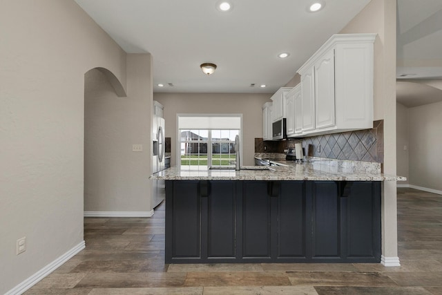 kitchen featuring a peninsula, backsplash, white cabinets, light stone countertops, and appliances with stainless steel finishes