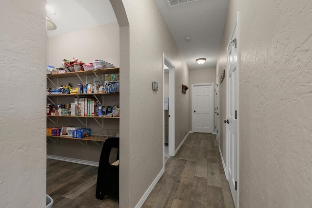 hallway featuring a textured wall, arched walkways, baseboards, and wood finished floors