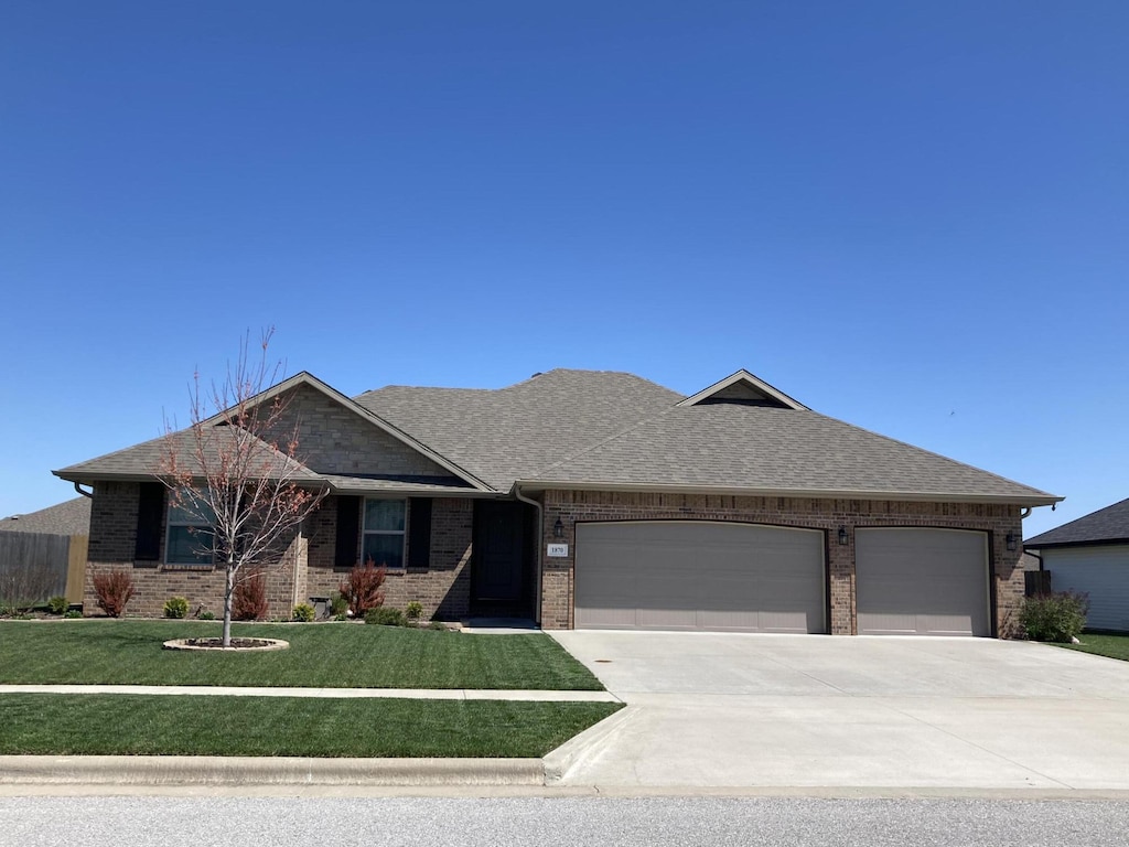 single story home featuring concrete driveway, a front lawn, an attached garage, brick siding, and roof with shingles