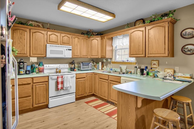 kitchen with a peninsula, white appliances, a kitchen bar, light wood-type flooring, and a sink