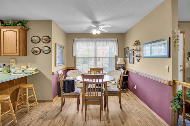 dining room with light wood-type flooring, a ceiling fan, baseboards, and a textured ceiling