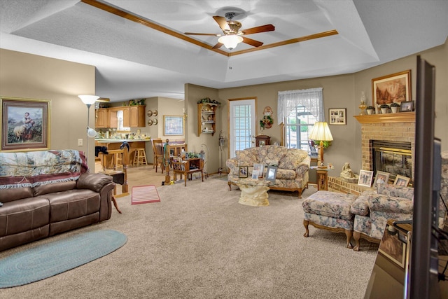 living area featuring a brick fireplace, carpet, a raised ceiling, and a ceiling fan