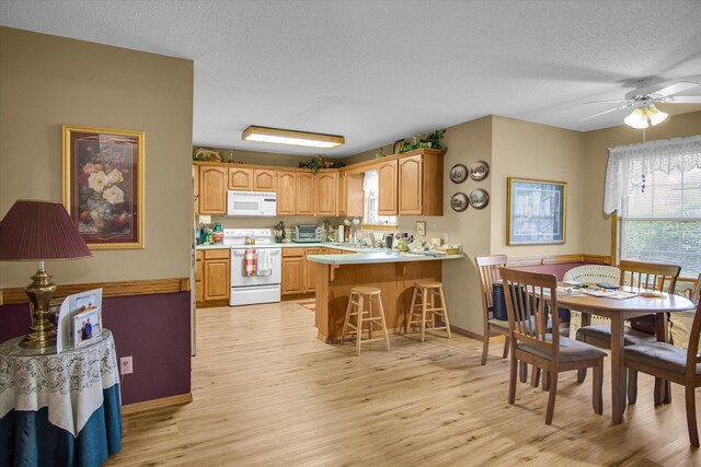 kitchen with white appliances, a peninsula, light countertops, and light wood-type flooring