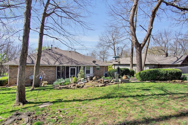 back of property with a yard, brick siding, a shingled roof, and a sunroom