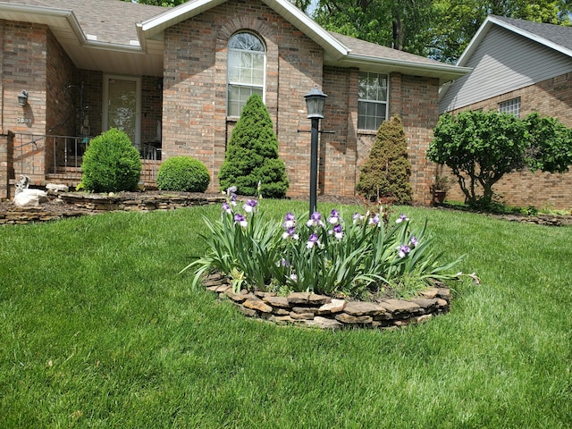 exterior space with roof with shingles, brick siding, and a front yard