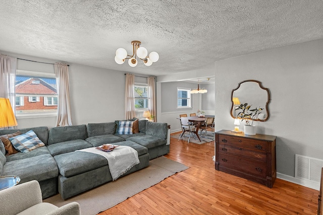 living room featuring light wood-style floors, plenty of natural light, a notable chandelier, and visible vents