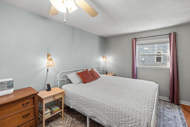 bedroom featuring a textured ceiling, wood finished floors, baseboards, and a ceiling fan