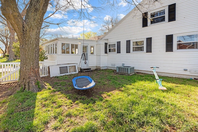 back of property with central AC, fence, and a lawn