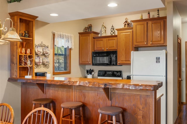 kitchen featuring freestanding refrigerator, a breakfast bar, brown cabinetry, black microwave, and stove