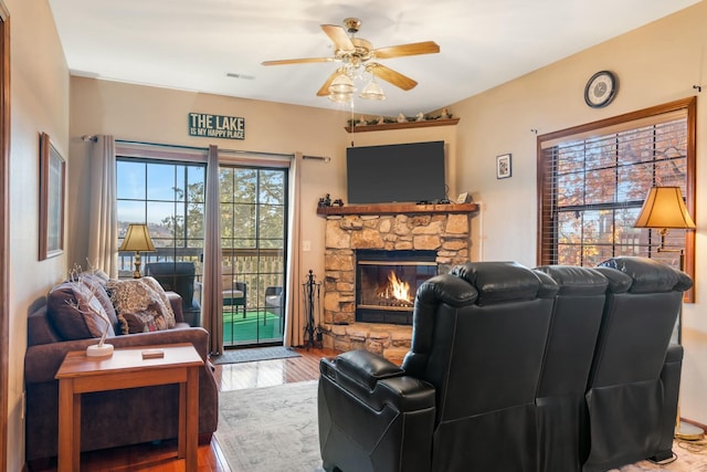 living area with wood finished floors, visible vents, a ceiling fan, and a stone fireplace