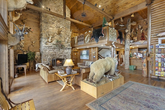 living area with log walls, a towering ceiling, a stone fireplace, hardwood / wood-style flooring, and wooden ceiling