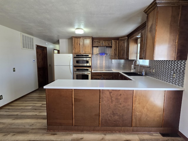 21282 County Road 295, Hermitage, MO 65668 - kitchen with a peninsula, a sink, visible vents, freestanding refrigerator, and wall chimney range hood