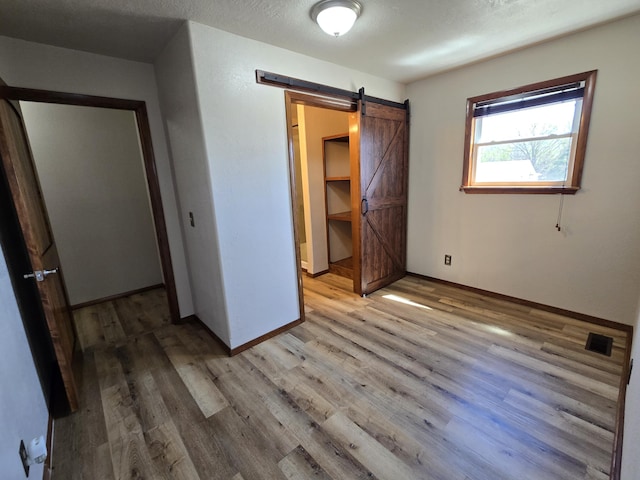 21282 County Road 295, Hermitage, MO 65668 - unfurnished bedroom with a barn door, light wood-type flooring, visible vents, and baseboards