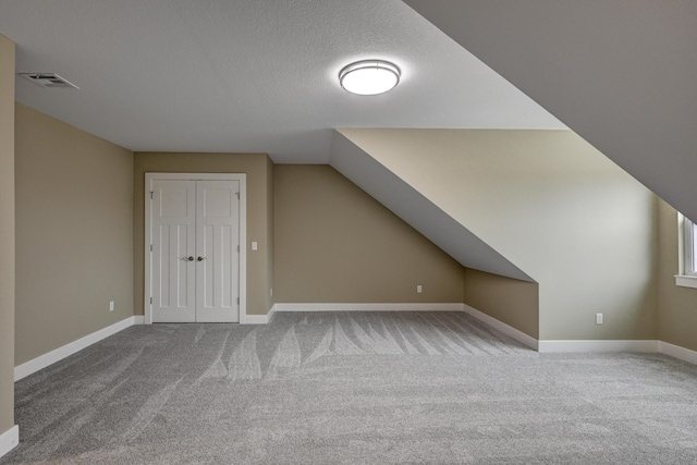 additional living space featuring visible vents, baseboards, a textured ceiling, carpet floors, and vaulted ceiling