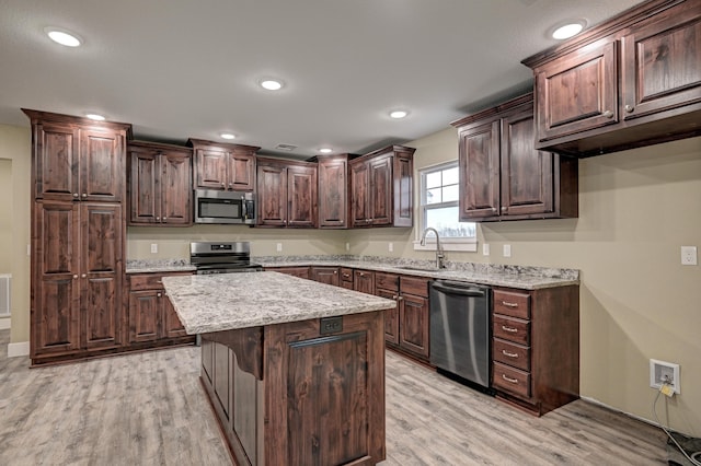 kitchen with a center island, a sink, appliances with stainless steel finishes, dark brown cabinetry, and light wood finished floors
